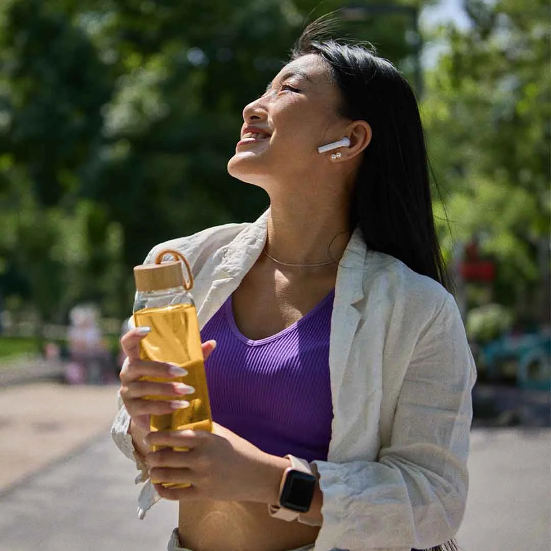Woman smiling outdoors, holding a bottle, wearing earphones and a smartwatch.