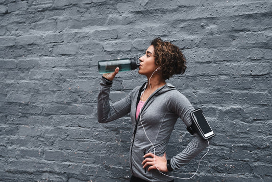 a woman drinking from a reusable water bottle next to a painted brick wall