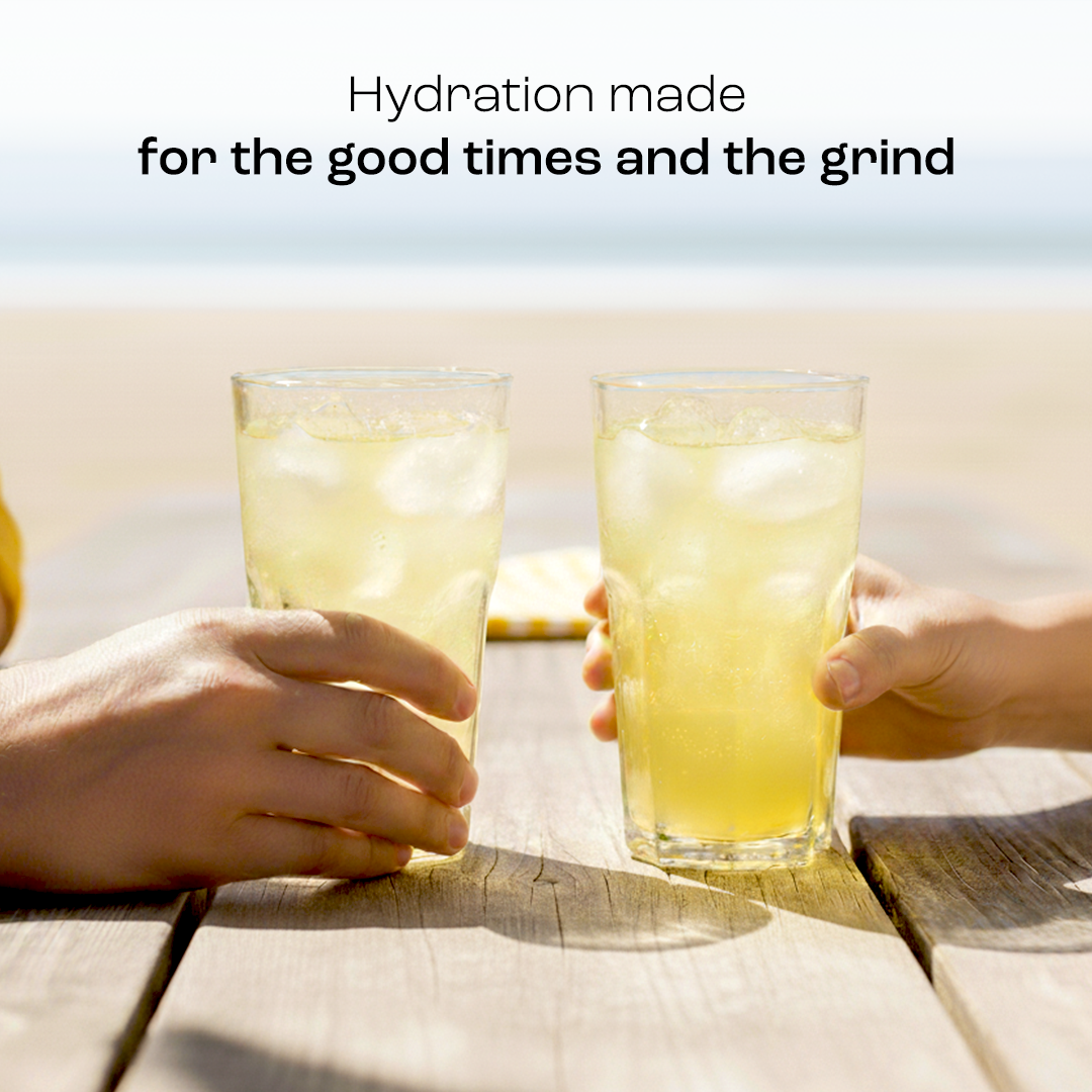 Two hands cheersing sugar-free Electrolyte Recovery Plus Powder drinks on the beach, mix text above.