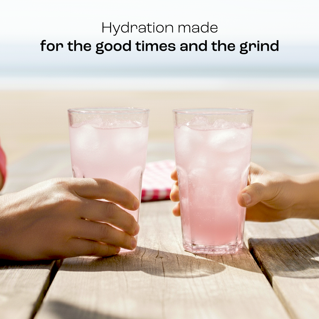 Two hands hold glasses of Electrolyte Recovery Plus Powder (Sugar-Free) at a sunny beach, text on hydration above.