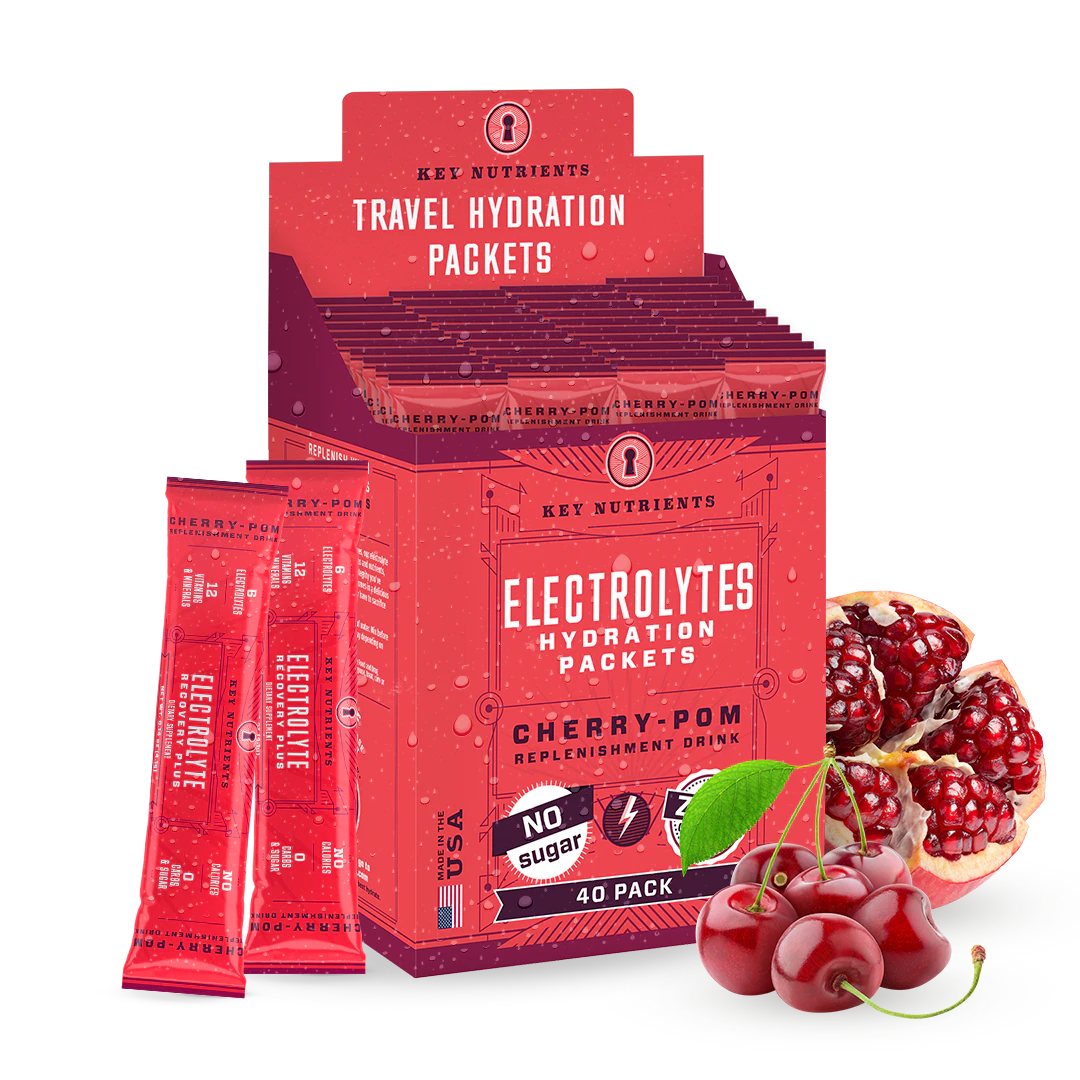 A box of Electrolyte Recovery Plus Powder (Sugar-Free) in red packaging is surrounded by vibrant cherries and juicy pomegranates, making it perfect for a refreshing hydration drink. Ideal for those on a keto diet, it promises to replenish and revitalize with every sip.