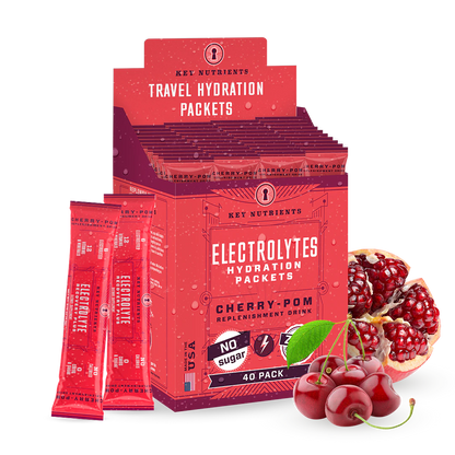 A box of Electrolyte Recovery Plus Powder (Sugar-Free) in red packaging is surrounded by vibrant cherries and juicy pomegranates, making it perfect for a refreshing hydration drink. Ideal for those on a keto diet, it promises to replenish and revitalize with every sip.